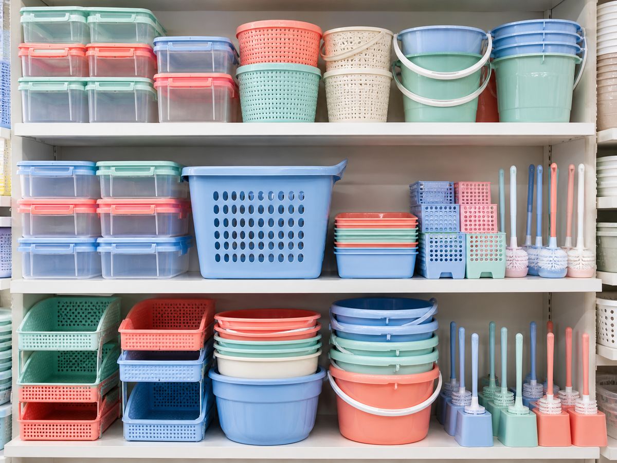 Pastel storage boxes, baskets, buckets and cleaning brushes arranged on white shelves